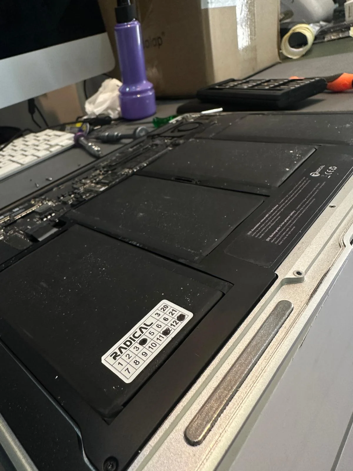 MacBook deschis pe masa de lucru, cu celulele bateriei la vedere